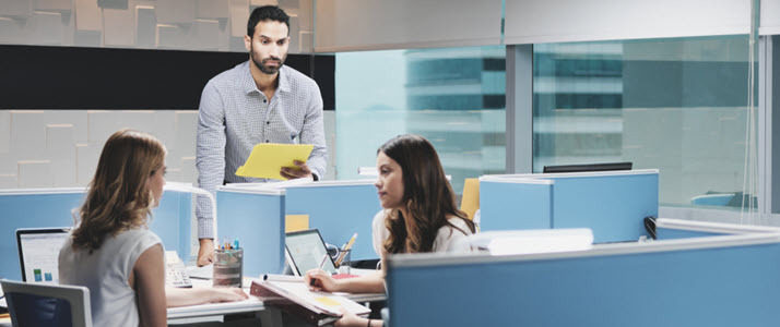standing man being ignored by female coworkers at nearby desk